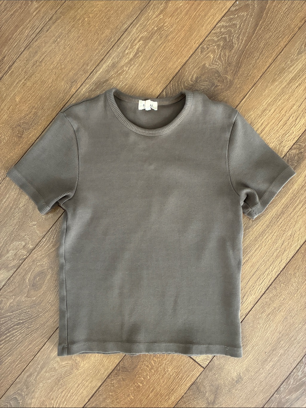 Grey ribbed plain baby tee laid flat on a wooden floor